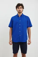 Camisa de manga corta azul con pequeños lunares blancos, cuello button-down y bolsillo en el pecho.
