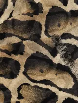 Bufanda rectangular con estampado de manchas tipo animal print en tonos marrón, beige y negro. Tiene flecos pequeños en los extremos.
