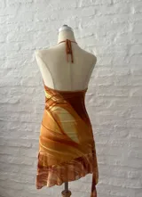 Vestido corto con estampado abstracto en tonos naranja, blanco y marrón. Diseño con escote halter y falda con volados.