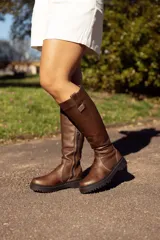 Bota de cuero color chocolate, de caña alta, con suela track y detalle de tira en la parte superior.