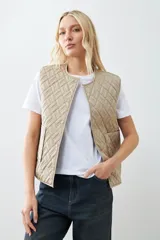 Chaleco capitoneado reversible a rayas azules y blancas con ribete color crema. Tiene cuello redondo, cierre con botones a presión y bolsillos de parche. El reverso es liso color tostado.