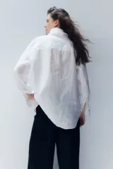 Camisa blanca de lino con cuello clásico, abotonada al frente, de manga larga con puños abotonados, canesú en la espalda, bolsillo de parche en el pecho y bajo redondeado.