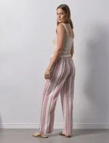 Pantalón de lino color blanco con rayas verticales rosas y celestes. Tiene pretina ancha elastizada con lazo de ajuste y bolsillos inclinados en la parte delantera.