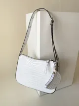 Cartera rígida de tamaño chico hecha en cuero, con asa regulable y detalles en ojalillos.
