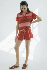 Short tejido en jersey color crudo con cintura elastizada azul marino y cordón rojo. Presenta rayas verticales rojas y laterales en azul marino.