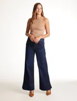 Jean wide leg azul oscuro de tiro alto, con pierna ancha y ruedo con tajo lateral. Presenta pretina con pasadores, botón y cierre, y bolsillos delanteros y traseros.