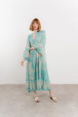 Vestido largo color celeste con estampado floral en tonos beige, escote en V, botonadura completa en el frente y mangas largas.