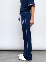 Pantalón de felpa azul marino, corte recto, con cintura elastizada y cordón ajustable. Presenta una franja blanca lateral y el escudo del Club Nacional de Football bordado en el muslo.