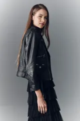 Campera de cuero ovino negra, estilo rocker, con cuello con solapas, cierre cruzado, cinturón ajustable en la cintura, charreteras en los hombros y múltiples cierres metálicos decorativos. Forro de poliéster.