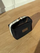 Neceser color beige de forma rectangular, con cierre superior y asa de mano.