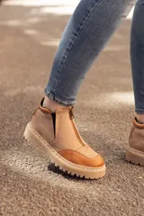 Bota de cuero color beige con puntera marrón, cierre frontal con cremallera y suela track.