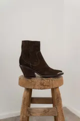 Bota corta de cuero gamuzado color marrón oscuro, con punta fina y detalle metálico. Tiene cierre lateral y taco de madera.