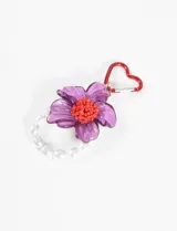 Llavero con dije de flor de acrílico color lila con centro naranja, argolla roja en forma de corazón y tira de perlas sintéticas.