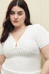 Top blanco con textura tramada, escote en V con leve frunce central, mangas cortas con elástico y volado sutil en el ruedo. Tejido con elasticidad.