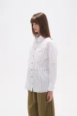 Camisa de algodón blanca, de corte ancho, con botones de madera y detalles de encaje calado en el frente, mangas y ruedo. Tiene cuello camisero y manga larga.