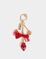 Llavero metálico dorado con dije de frutilla roja con incrustaciones blancas, moño de encaje rojo, dije con la palabra "Yummy!" y dije de corazón alado.