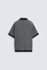 Polo de hombre de corte relajado, tejido de punto de algodón a rayas verticales en tonos gris y negro. Tiene cuello solapa, cierre frontal con botones y mangas cortas.