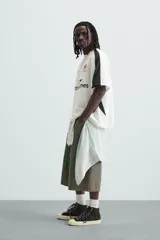 Camiseta blanca de corte holgado con mangas cortas negras. Presenta un logo azul en el pecho izquierdo, un escudo rojo con un caballo en el pecho derecho y la inscripción "Victory Games" en negro en el centro.