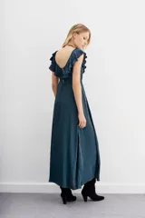 Vestido largo negro sin mangas, con escote redondo, espalda baja y volados en el escote. Ajuste en la cintura con cordón y terminaciones metálicas.