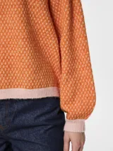 Suéter de punto jacquard color naranja con cuello redondo y ribetes en rosa.