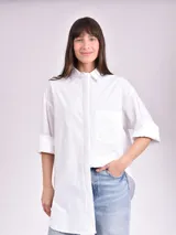 Camisa blanca de corte amplio, con cuello clásico, mangas 3/4 con puños arremangados y bolsillo de parche en el pecho.