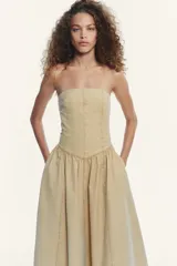 Vestido midi color beige, de corte recto, con escote palabra de honor y hombros descubiertos. Confeccionado en tejido con efecto lavado y detalle de pliegues. Cierre trasero con cremallera metálica.