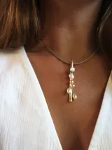 Collar con cordón fino color beige y dije vertical de bronce con perlas blancas de diferentes tamaños.