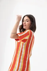 Vestido corto tejido calado a rayas horizontales en tonos naranja, amarillo y blanco, con cuello tipo polo y cierre frontal con botones.