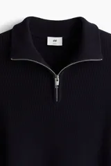 Buzo de punto fino color azul marino, de corte ajustado, con cuello alto y medio cierre frontal con cremallera metálica.
