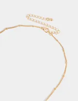 Collar corto dorado con cadena de eslabones y dijes colgantes: moneda dorada con letras NY grabadas, dos manzanas rojas esmaltadas y dije redondo dorado con corazón rosa.