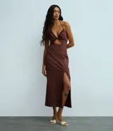 Vestido midi color marrón oscuro, con escote halter y detalle de lazo en el cuello. Presenta un fruncido en el busto con un corte tipo cutout en la zona del abdomen y una abertura lateral en la falda.
