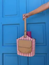 Matero tipo balde con cuerpo de tela a rayas verticales blancas y celestes pálidas. Posee un bolsillo frontal de símil cuero color camel con solapa y logo grabado. Incluye asa de mano y correa larga desmontable.