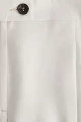 Pantalón sastrero color beige de sarga con pinzas, corte holgado, tiro alto, pretina prolongada con botón, bolsillos al bies y bolsillos insertados atrás. Piernas anchas con pliegues adelante y atrás.