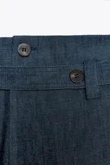 Pantalón de tiro medio azul denim, con trabillas en la cintura y cinturón ajustable con botones. Tiene bolsillos laterales ocultos y pierna ancha.