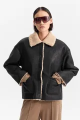 Campera corta de efecto cuero negro, con forro y cuello de corderito color beige. Cierre frontal mediante botones y bolsillos amplios.