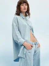 Camisa celeste de denim con botones marrones, corte holgado y mangas largas.