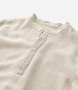 Camisa blanca de manga larga, corte amplio y cuello padre (mandarín). Presenta un frente abotonado con tapeta corta.