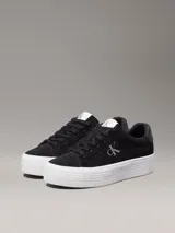 Zapatillas de ante negras con plataforma blanca y logo CK en el lateral.
