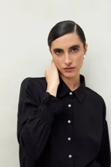 Camisa negra de manga larga con cuello clásico y botones frontales. El tejido presenta una textura arrugada o plisada, y los puños tienen un detalle fruncido o elástico.