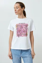 Remera blanca de algodón con estampado de flores rosadas y texto 'LET LOVE IN'.