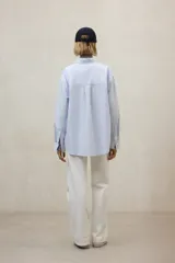 Camisa de algodón a rayas verticales finas celestes y blancas, con cuello clásico y corte holgado.