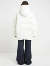 Campera oversize color blanco, confeccionada en nailon suave con un leve brillo. Cuenta con capucha, bolsillos laterales con cremallera, relleno natural y ajuste inferior con cordón. Presenta cierre frontal con cremallera de doble cursor y diseño acolchado.