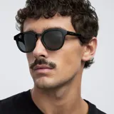 Lentes de sol negros con montura redonda de diseño angular y detalles geométricos. Lentes polarizadas alemanas con protección UV400, recubrimiento anti-scratch y superhidrofóbico. Fabricados con material bio-based G850 y patillas de propionato de celulosa.