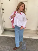 Camisa blanca de algodón con corte amplio y mangas largas. Presenta detalles en rojo en cuello, bolsillo y puños con terminaciones fruncidas.