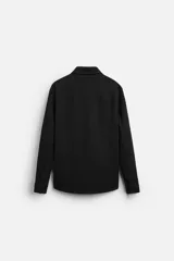 Sobrecamisa negra de tejido con elasticidad, cuello solapa y manga larga acabada en puño con botón a presión. Tiene bolsillos de plastrón en el pecho y cierre frontal con botones a presión.