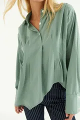 Camisa color crema de algodón, con cuello polo, mangas largas con puños abotonados y corte asimétrico.