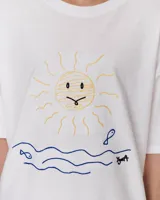 Remera blanca de corte holgado con estampado de un sol, olas y peces.