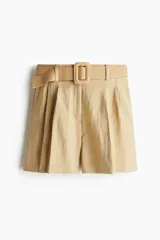 Short color beige de corte holgado con tiro alto, bolsillos laterales discretos, bolsillos atrás insertados y cierre con botón y corchete ocultos. Piernas con pinzas y pliegues adelante y atrás. Incluye cinturón ancho extraíble de rafia con hebilla cuadrada.