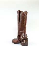 Bota de cuero marrón con caña alta, taco de madera y arnés con hebillas metálicas.