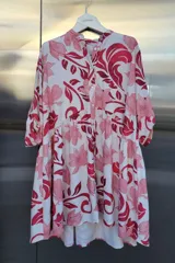 Vestido corto con estampado floral en tonos rosa y rojo. Tiene cuello mao, botones en el frente, corte con volados y mangas tres cuartos.